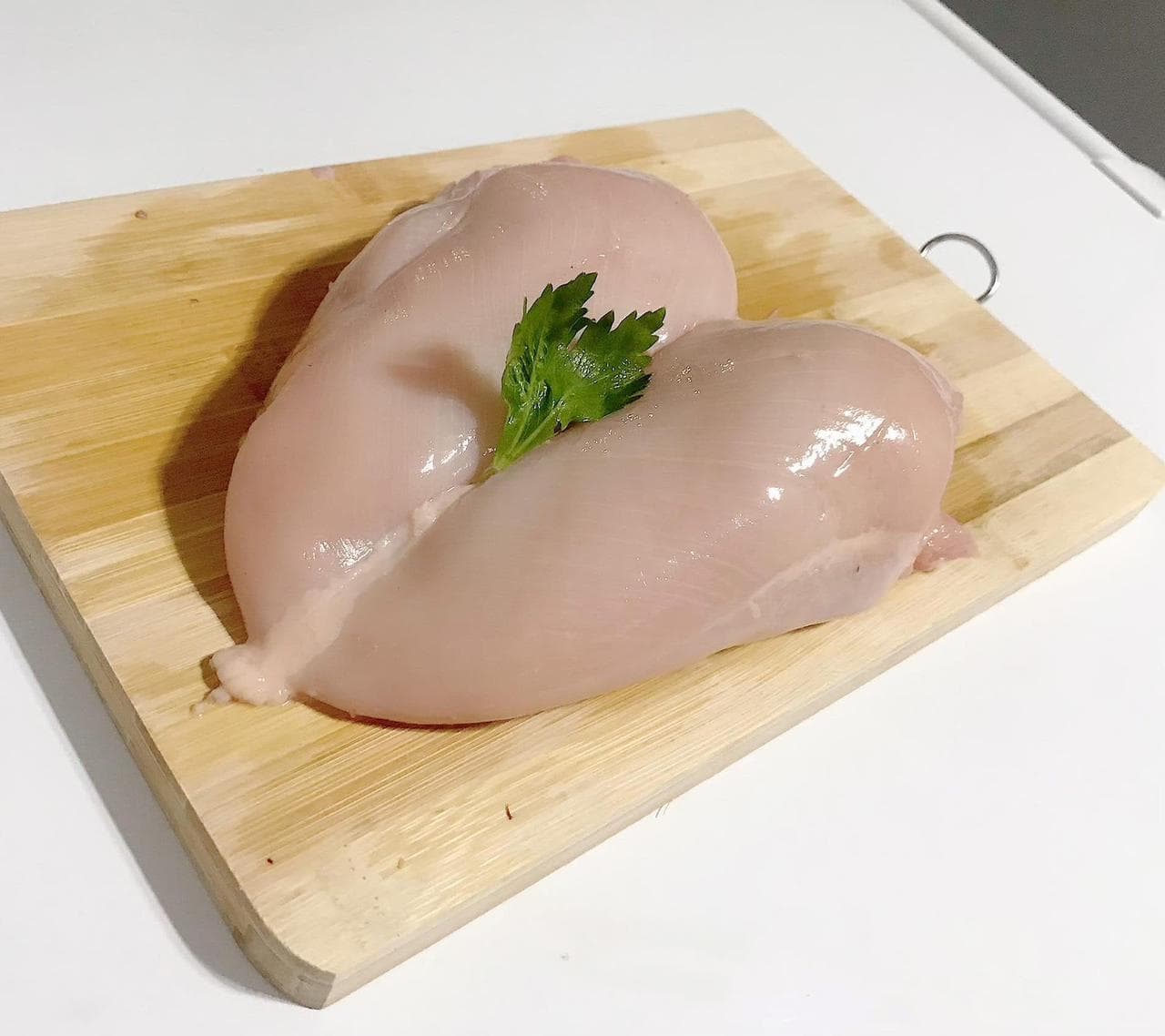 Two trimmed boneless chicken breast fillets on a wooden board
